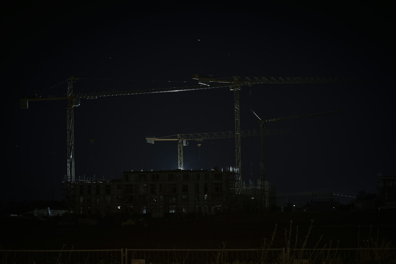 Baustelle mit Kränen bei Nacht, nur von Straßenlaternen beleuchtet